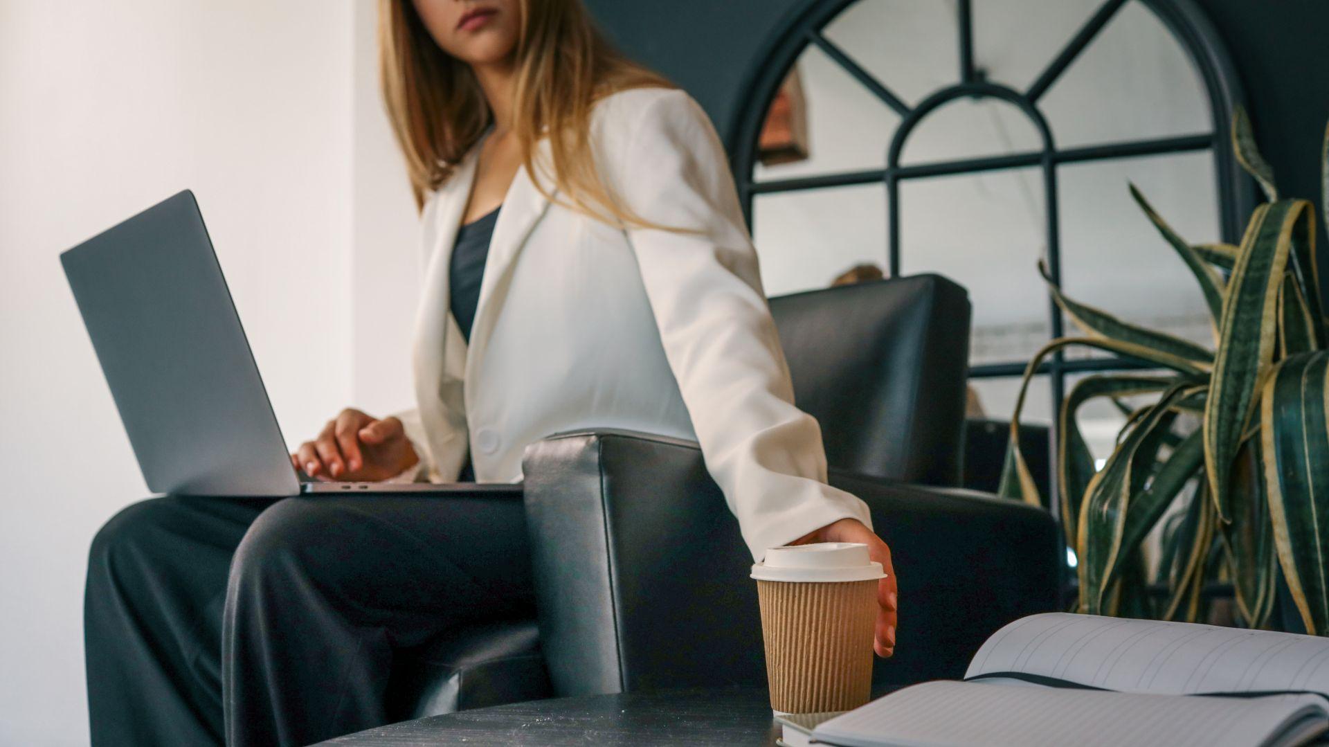 Woman with laptop and coffee in modern office – represents productivity and professional support from an onlyfans manager